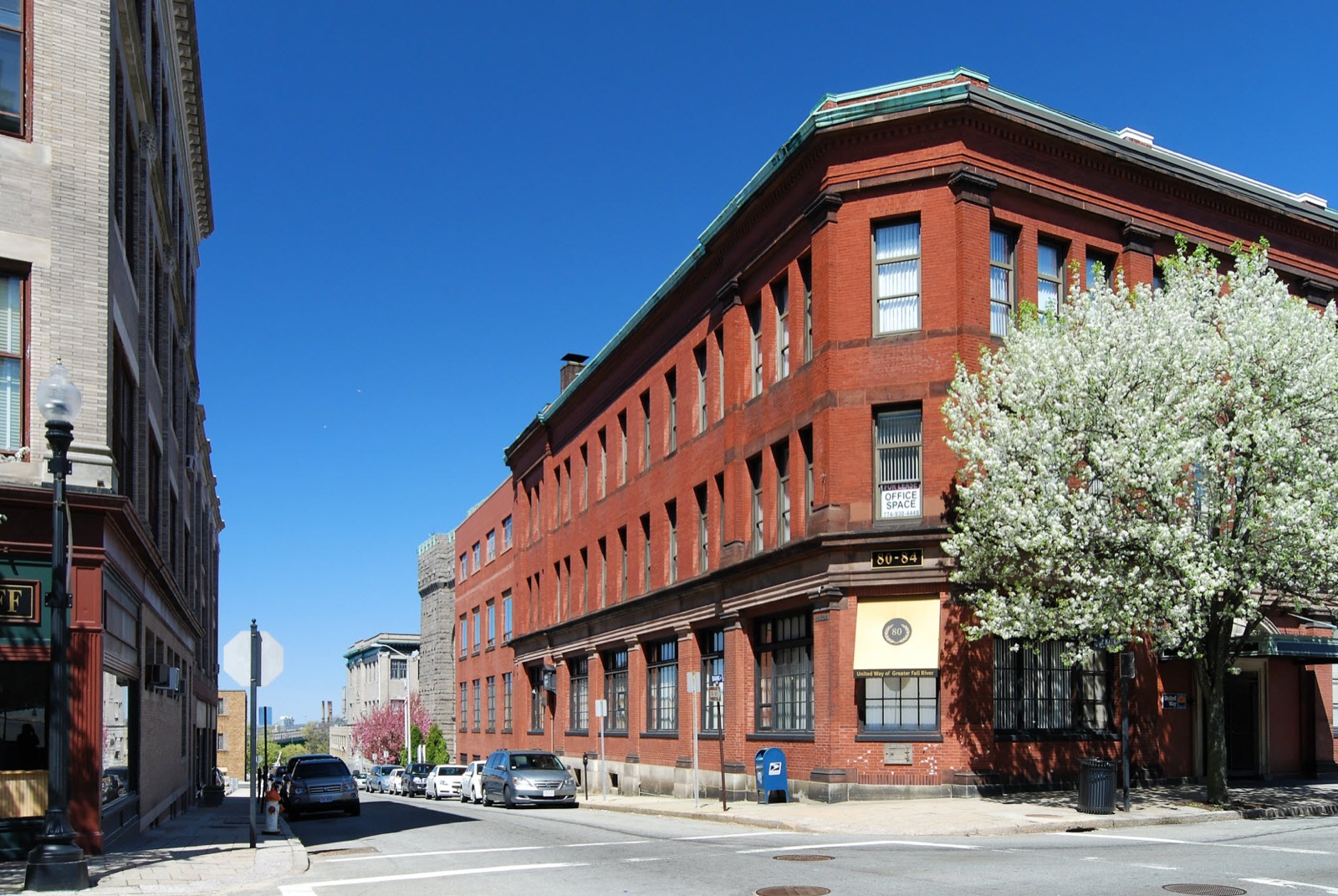 Red brick buildings on Bank Street in downtown Fall River, Massachusetts, with a flowering tree on the corner