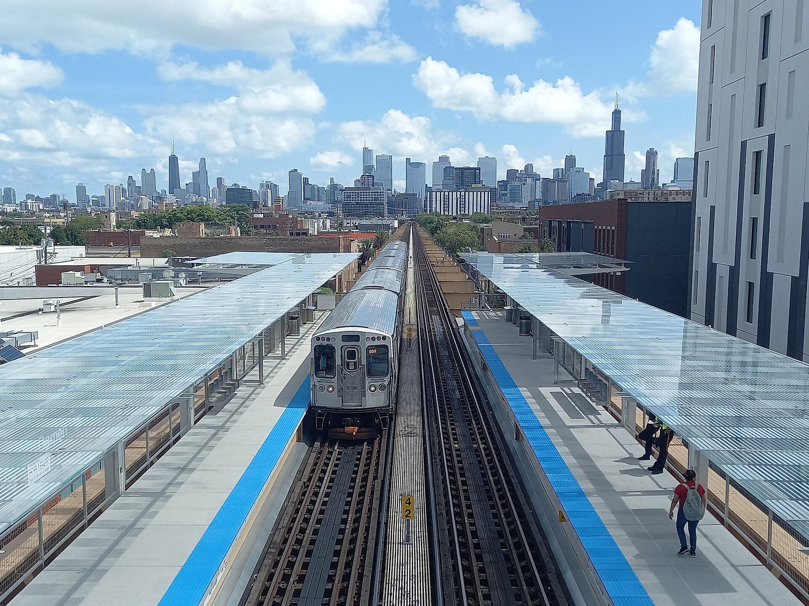 A CTA Green Line train at the Damen station platform with the Chicago skyline behind it