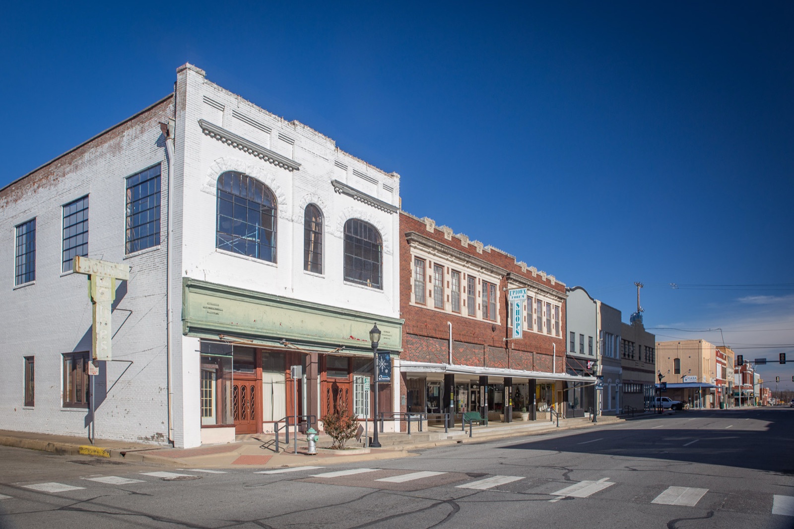 Two-story brick and white storefront buildings on a street corner in downtown Greenville, Texas