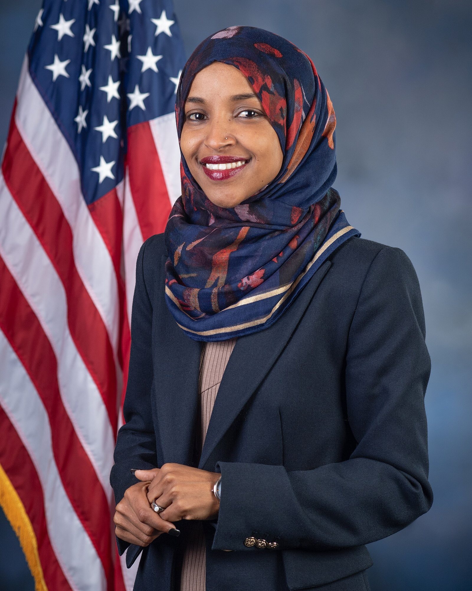 Rep. Ilhan Omar in her official congressional portrait, standing in front of a U.S. flag