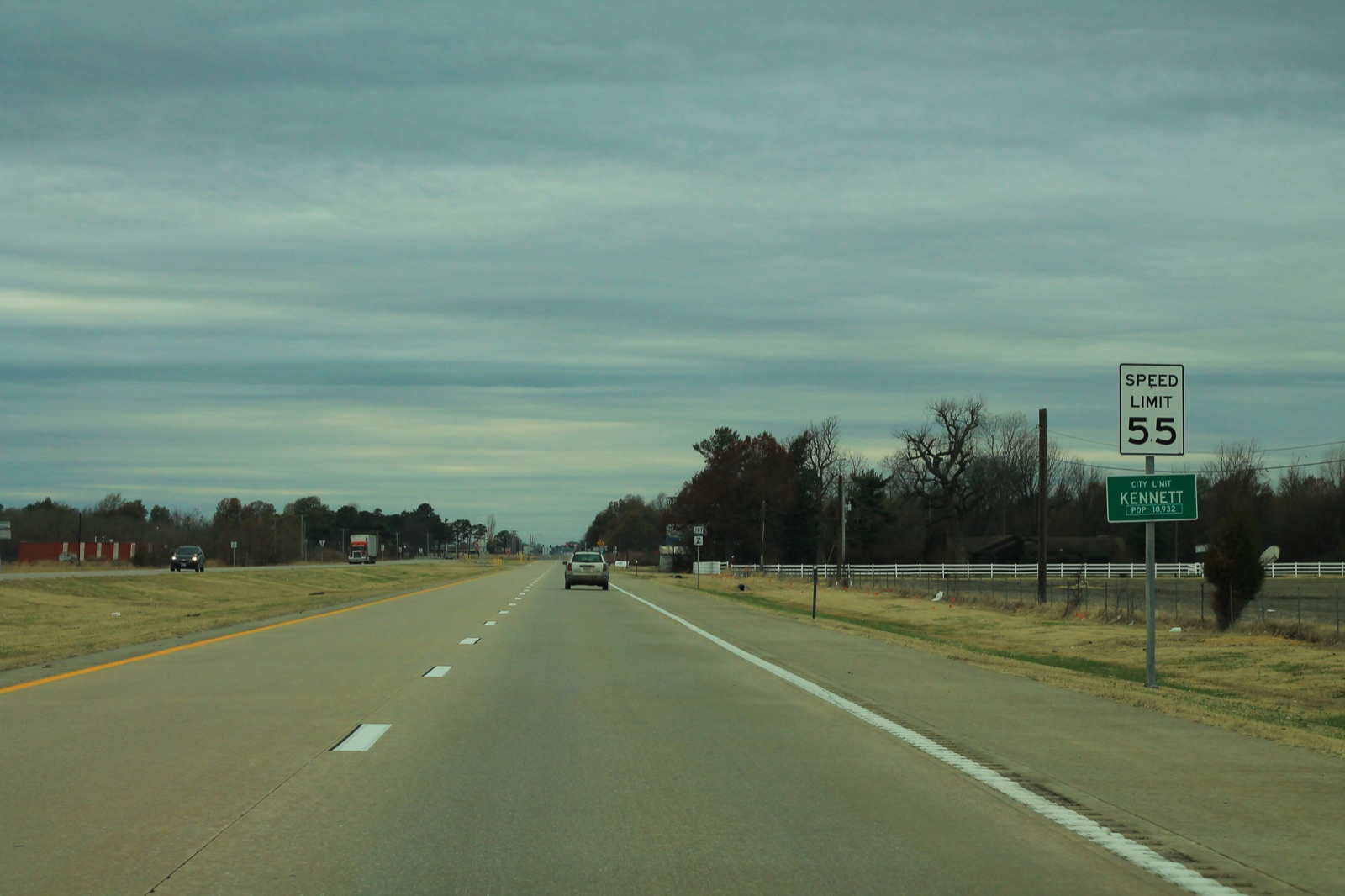 A two-lane highway with a speed limit sign and a green Kennett city limit sign under a cloudy sky
