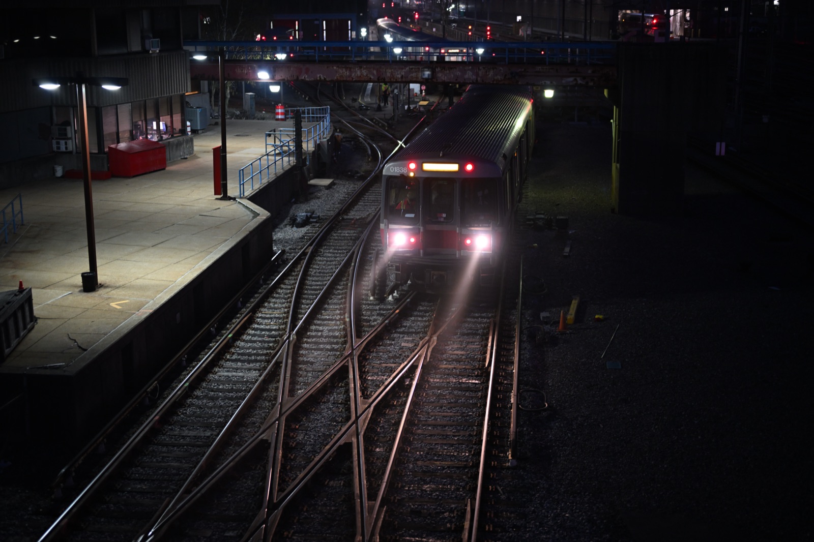 An MBTA Red Line train with its headlights on moving along tracks at Cabot Yard at night