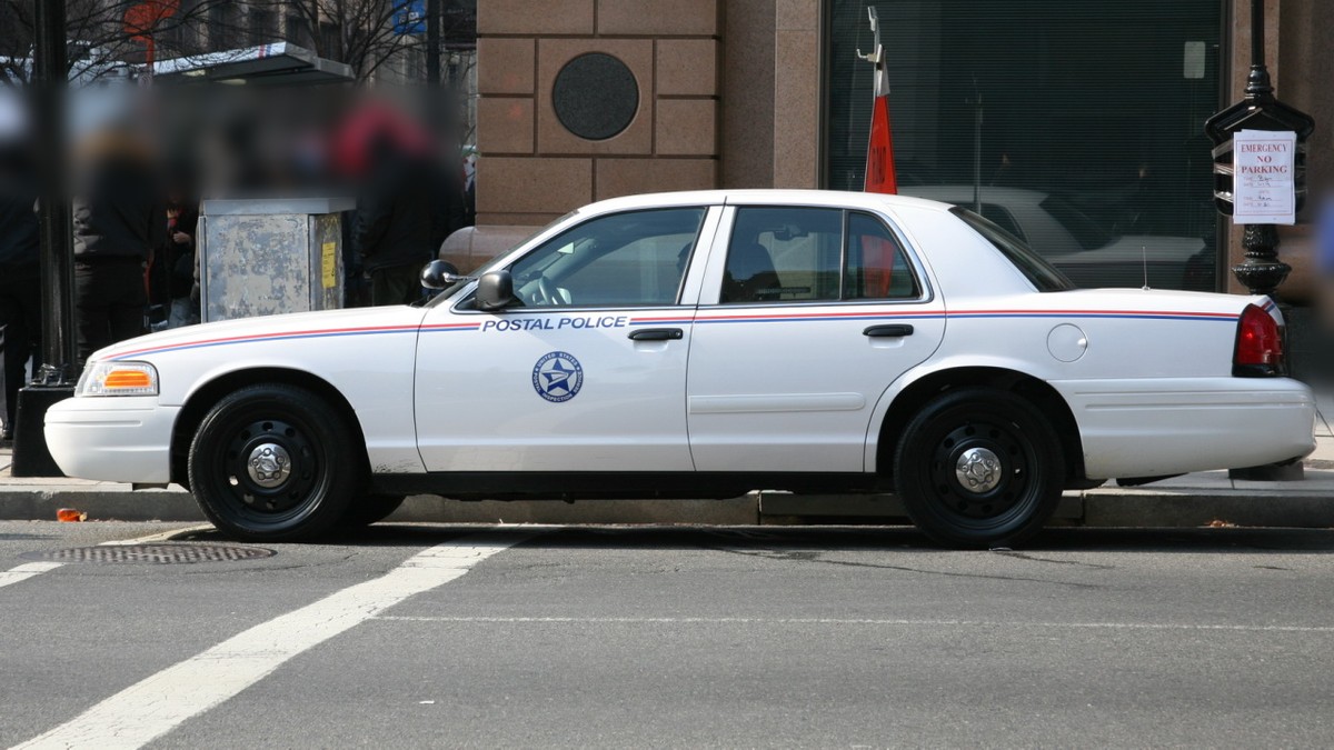 A white U.S. Postal Police car with the Postal Inspection Service emblem parked on a city street