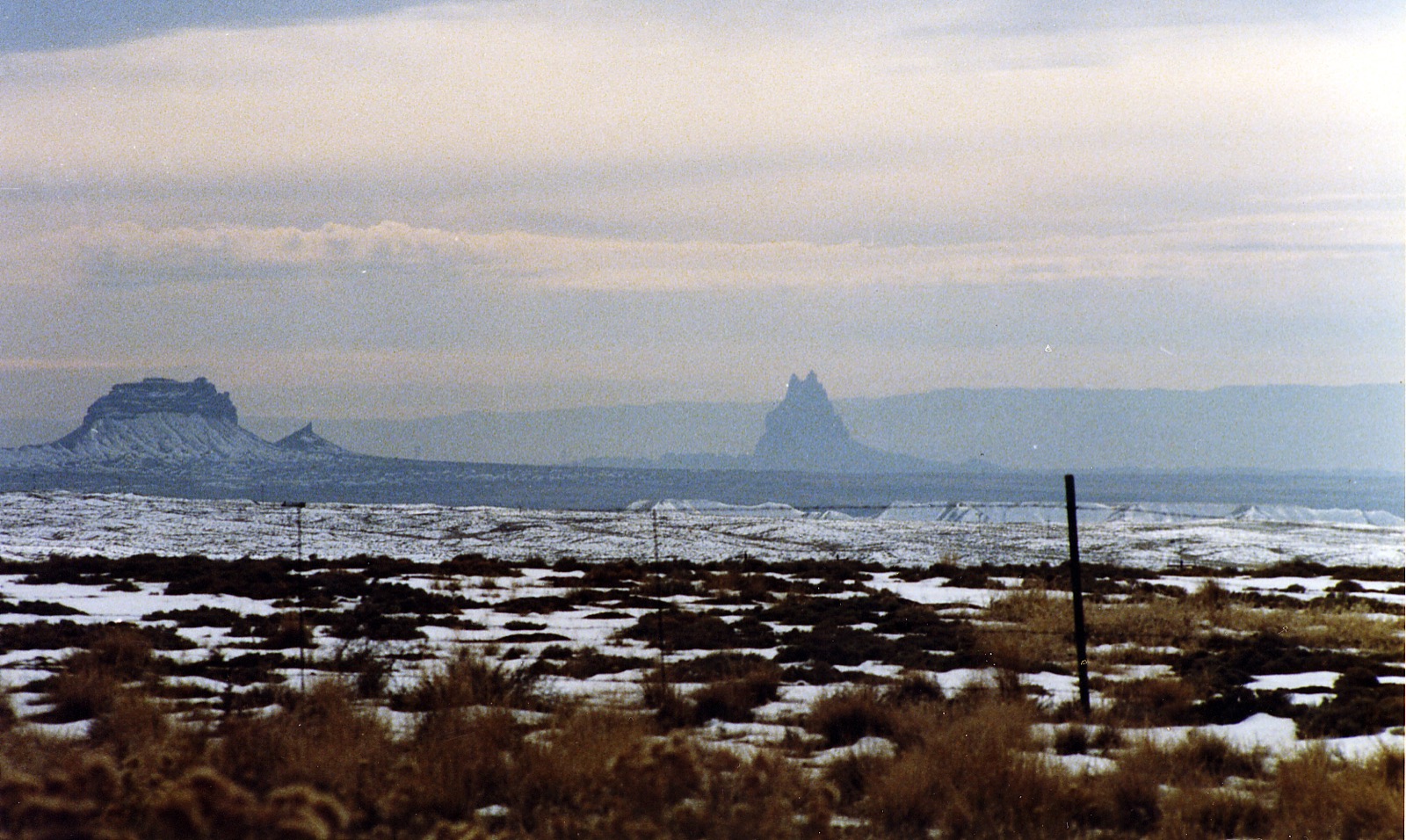 The Shiprock rock formation rising on the horizon above snowy desert scrubland in New Mexico